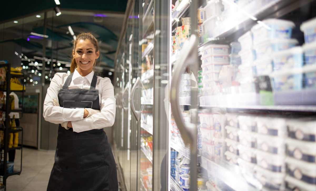 mulher ao lado de refrigerador fazendo gestão de estoque em supermercados